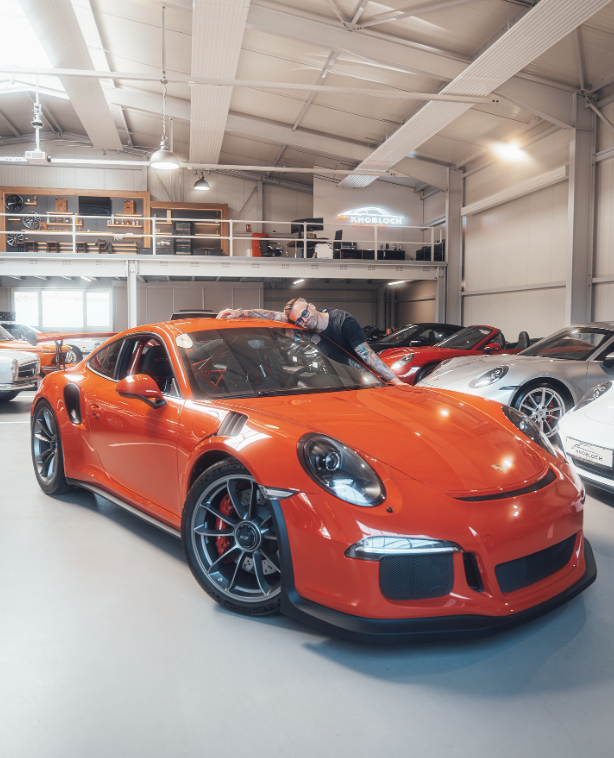 Sven Knobloch legt seinen Kopf auf einen orangenen Porsche