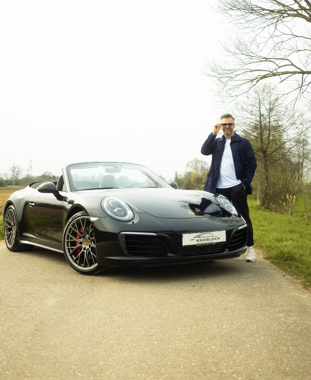 Sven Knobloch steht auf einem Feldweg neben einem schwarzen Porsche Cabrio